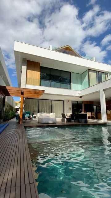 Modern two-story house with large glass windows, wooden deck, outdoor furniture, and swimming pool
