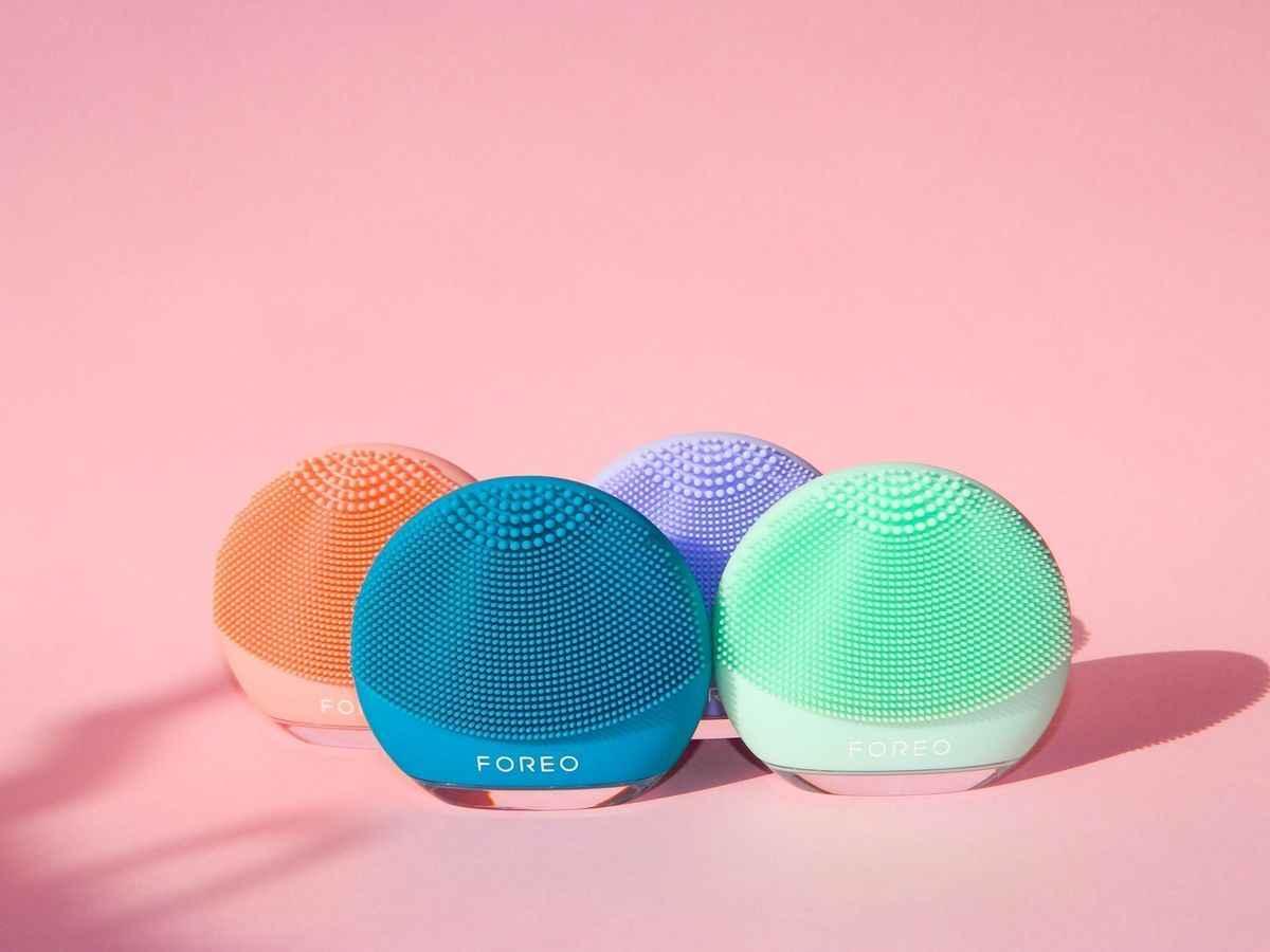 Four colorful Foreo facial cleansing silicone brushes on pink background