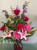 Mixed flower bouquet with red roses, pink lilies, purple flowers, and greenery in a red vase