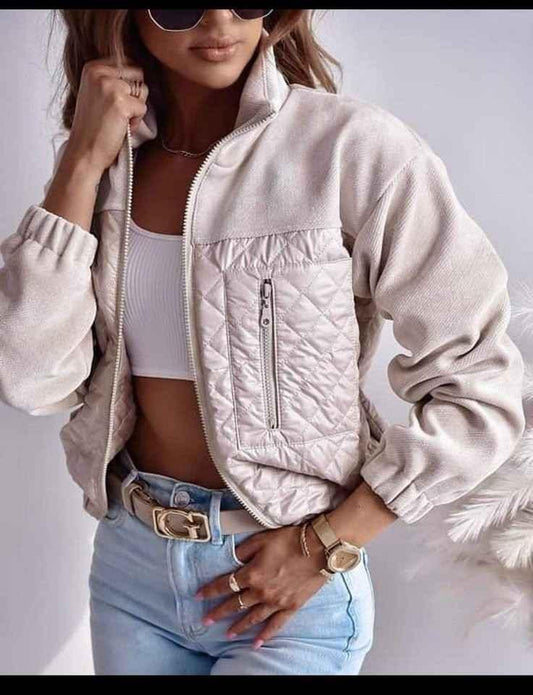Woman wearing light beige quilted zip jacket with high collar, white crop top, blue jeans, gold watch, and belt