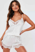 Woman wearing white lace trim camisole and shorts pajama set on white background