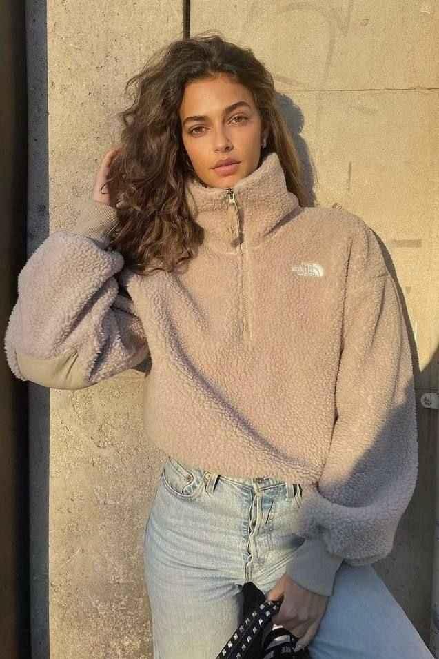 Woman wearing beige The North Face fleece jacket and light blue high-waisted jeans against stone wall