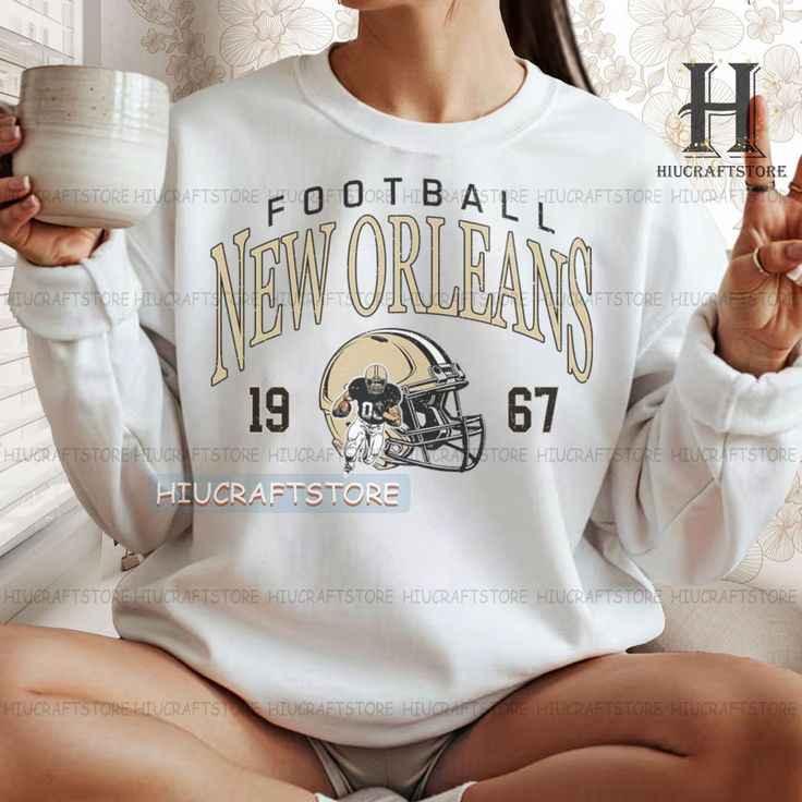 Woman wearing white New Orleans football sweatshirt with 1967 graphic, holding white mug