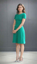 Woman in a green textured dress and patterned high heels standing against a gray wall