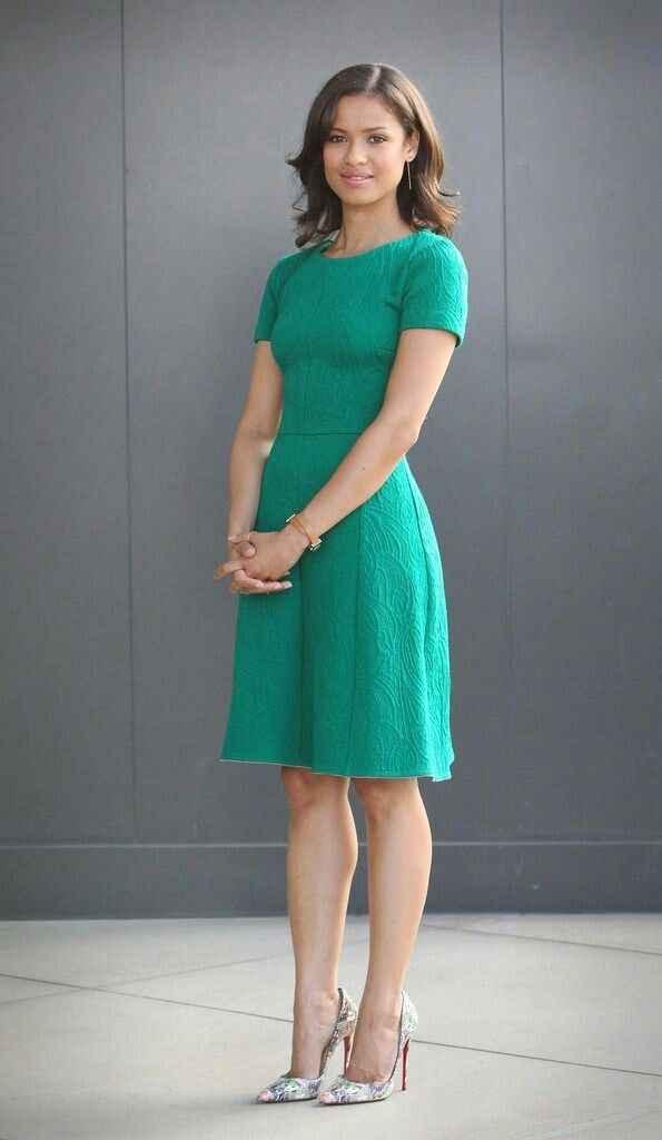 Woman in a green textured dress and patterned high heels standing against a gray wall