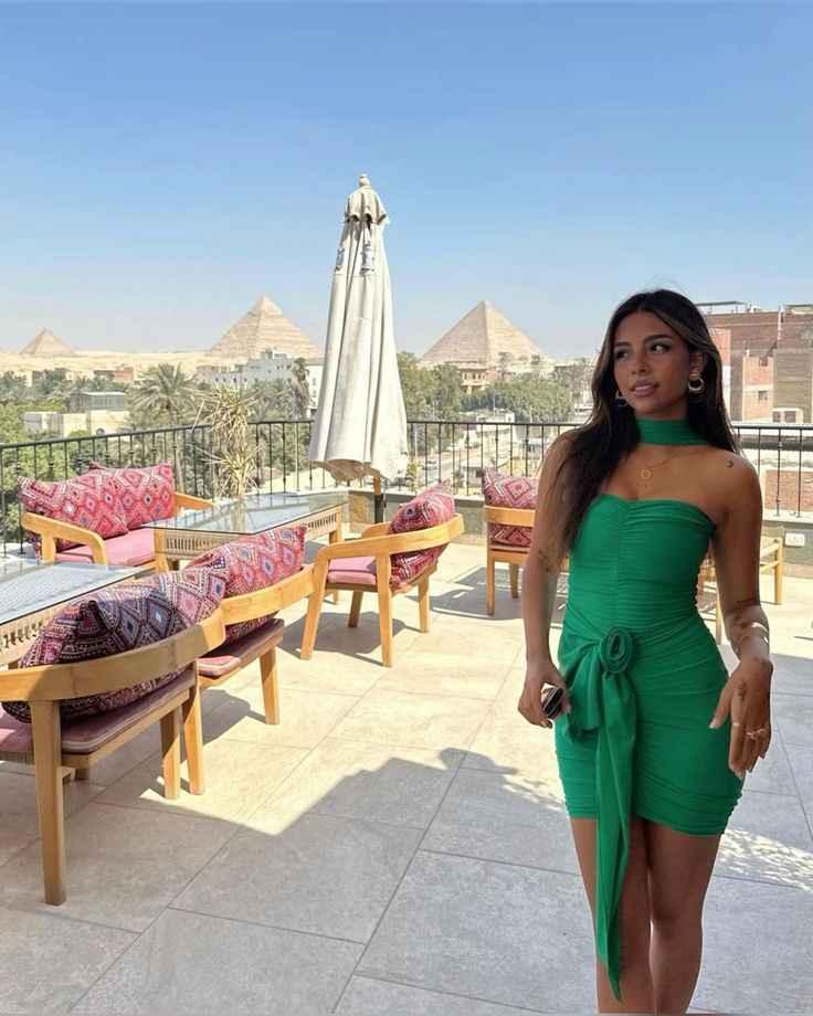 Woman in green dress on rooftop terrace with wooden furniture and Great Pyramids in background