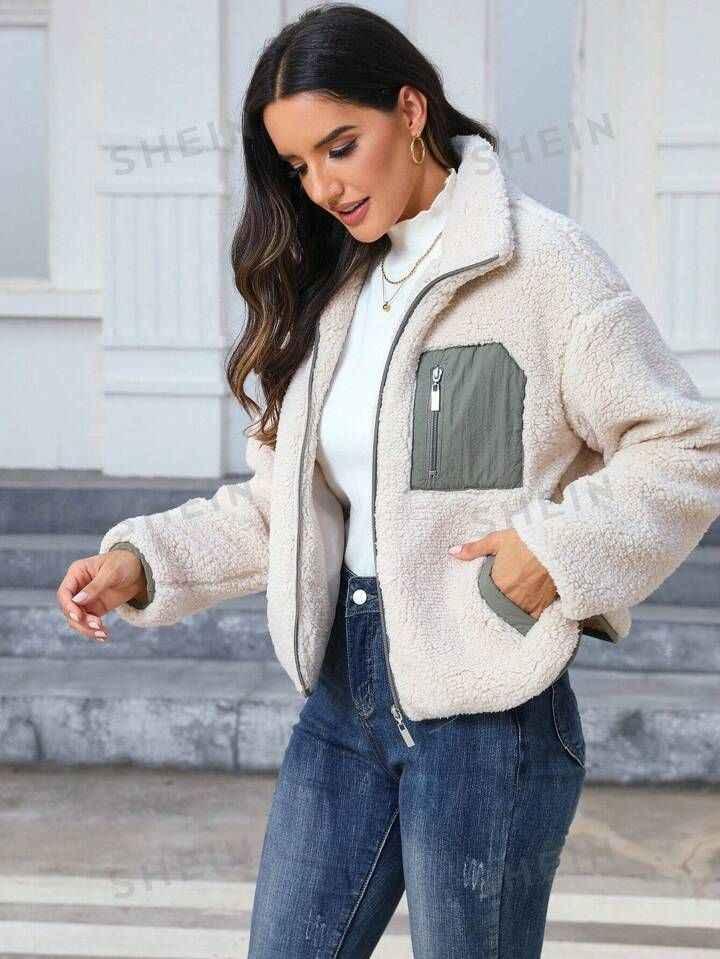 Woman wearing beige sherpa fleece jacket with gray zip pocket, white top, and blue jeans outdoors