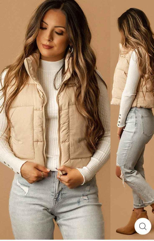 Woman wearing beige puffer vest over white ribbed sweater with ripped light wash jeans and ankle boots