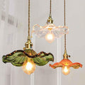 Three vintage glass pendant lights with ruffled shades in green, clear, and orange hanging indoors