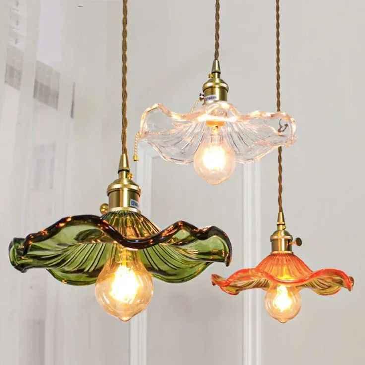 Three vintage glass pendant lights with ruffled shades in green, clear, and orange hanging indoors