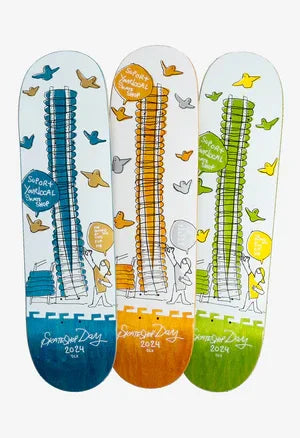 Three colorful skateboard decks featuring tall building illustration with flying birds and cartoon characters holding balloons, labeled 'SurfArt Skateboard Shop Summer Day 2024'