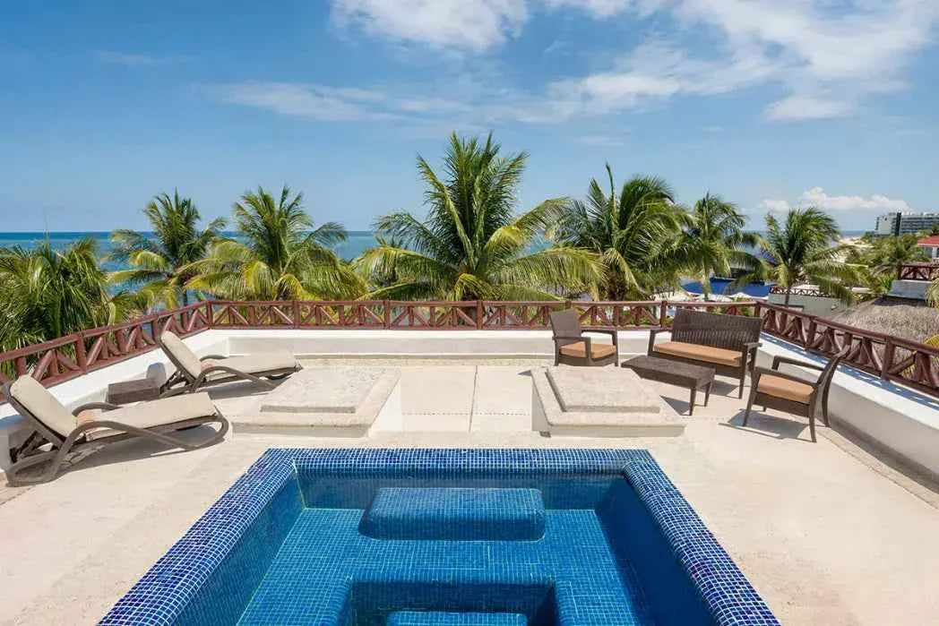 Rooftop terrace with blue-tiled jacuzzi, lounge chairs, seating area, palm trees, and ocean view