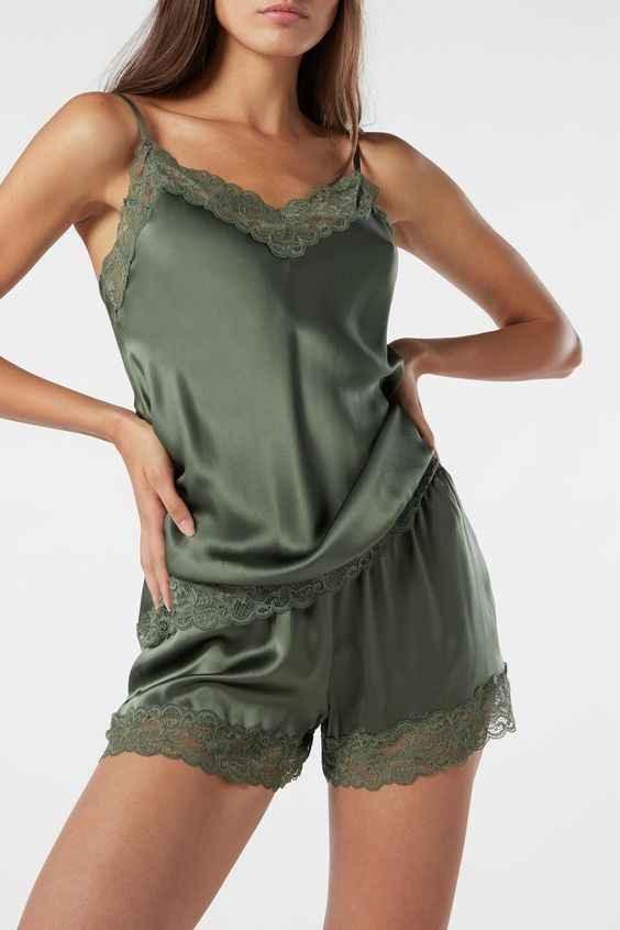 Woman wearing green satin camisole and shorts set with lace trim, posing against white background