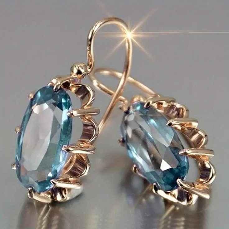Gold earrings with large oval blue gemstones in ornate prong settings on gray surface