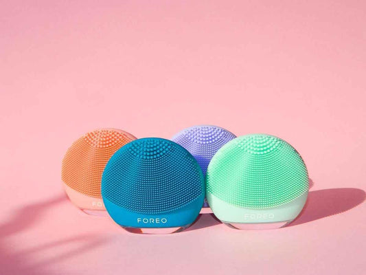 Four colorful Foreo facial cleansing silicone brushes on pink background