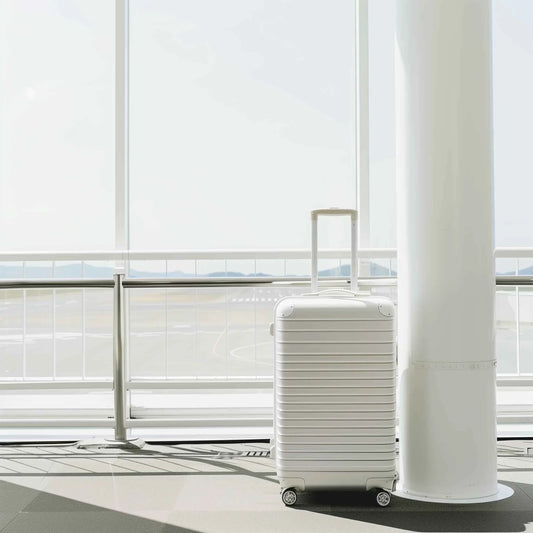 White hard-shell suitcase with wheels and handle standing by white pillar in bright modern airport terminal