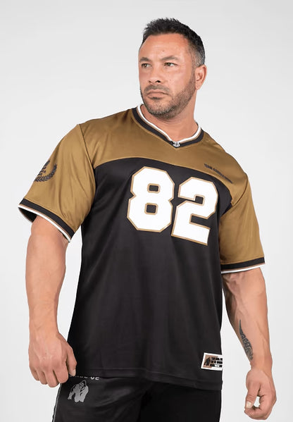 Man wearing black and gold sports jersey with number 82, standing against white background